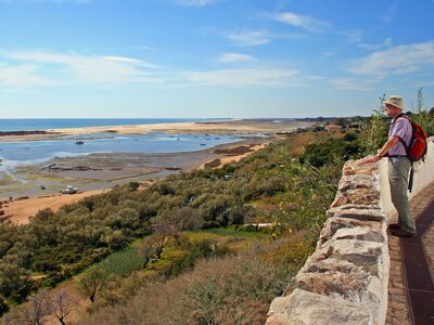 Coastline view of Tavira being admired by male walker standing next to stone wall, Portugal