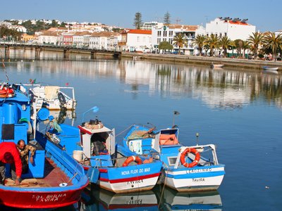Sailers on docked boat in Tavira with distant buildings reflecting in calm water, Portugal