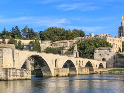 Low water-level view of Avignon Bridge with reflection across water and Popes Palace in distance during sunny day, Pont Saint-Benezet, Provence, France
