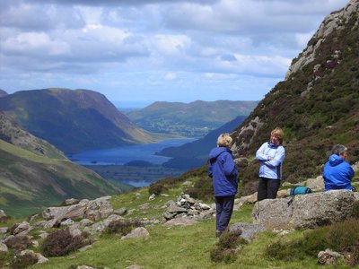 Three walkers having a break by rock amidst hills with views of Derwentwater and Buttermere in background