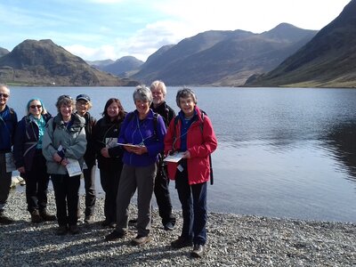 Group of people holding maps while standing on shoreline next to lake in the Lake District, Cumbria