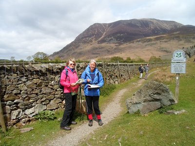 TTwo women holding maps standing next to The National Trust Rannerdale signpost, with Rannerdale Knotts nearby and two people in distance looking over
