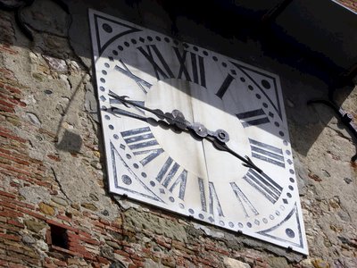 Roman numeral clock on stone wall building showing time - quarter to four, Anghiari, Italy