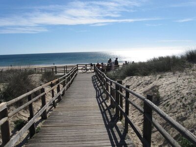 Wooden decking pathway leading towards Monte Gordo beach and sun shining across sea, Portugal