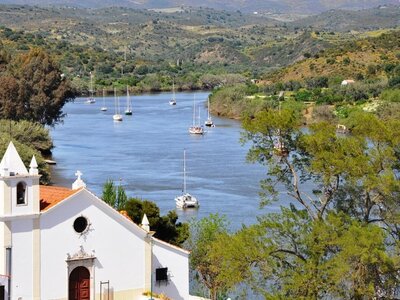 High view of Alcoutim with church in foreground and sailboats in distance on Guadiana river, Portugal
