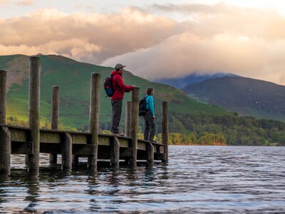 Two walkers standing on wooden dock at Derwentwater in Lake District during sunrise