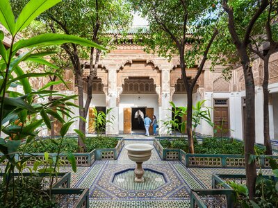 Garden area with tall trees and green plants surrounded by mosaic patterned tiles in Bahia Palace, Marrakesh, Morocco