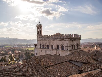 High view of Palazzo dei Consoli with sun shining through clouds above, Gubbio, Italy