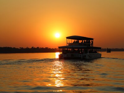 Orange sunset reflecting across the water of Zambezi River with silhouette of people on boat cruise enjoying view, South Africa