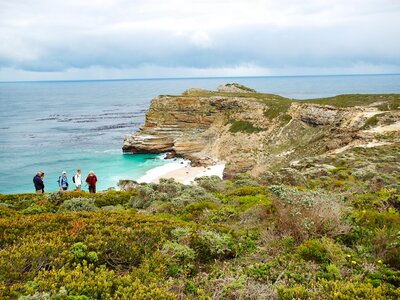 Ramble Worldwide walking group at Cape of Good Hope surrounded by colourful fauna shrubbery at Atlantic coastal edge near turquoise waters of South Africa