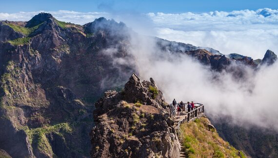 People trekking from Pico do Arieiro to Pico Ruivo standing at viewpoint surrounded by mountain landscape and clouds, Madeira island, Portugal
