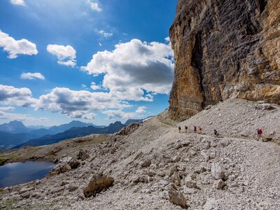 Group of walkers passing through the rocky foothills below a cliff in the Dolomites, Italy