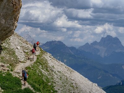 A walking group  in the Dolomites, Italy, on a narrow path, cresting a rise with peaks in the distance